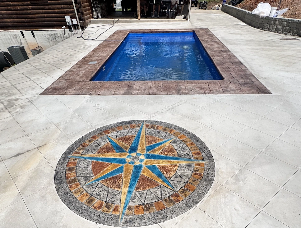 Hand-coloured compass rose medallion stamped into a concrete pool deck in blue, gold and rust tones &mdash; The Concord Concrete Company