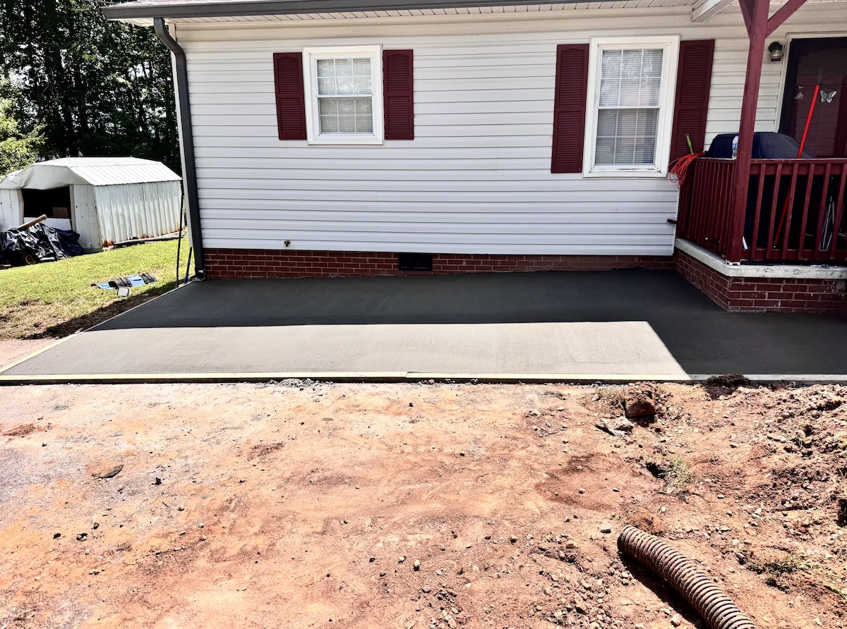 Freshly poured broom-finished concrete driveway extension beside a white ranch home, timber edge form still in place &mdash; The Concord Concrete Company