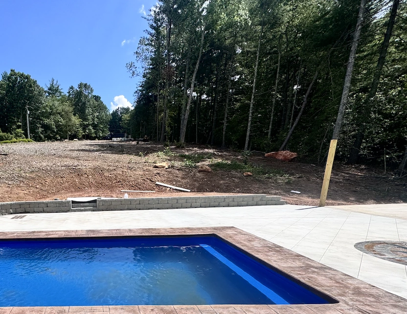 Concrete pool deck with a segmental block retaining wall holding a freshly graded slope at a wooded NC Foothills property &mdash; The Concord Concrete Company