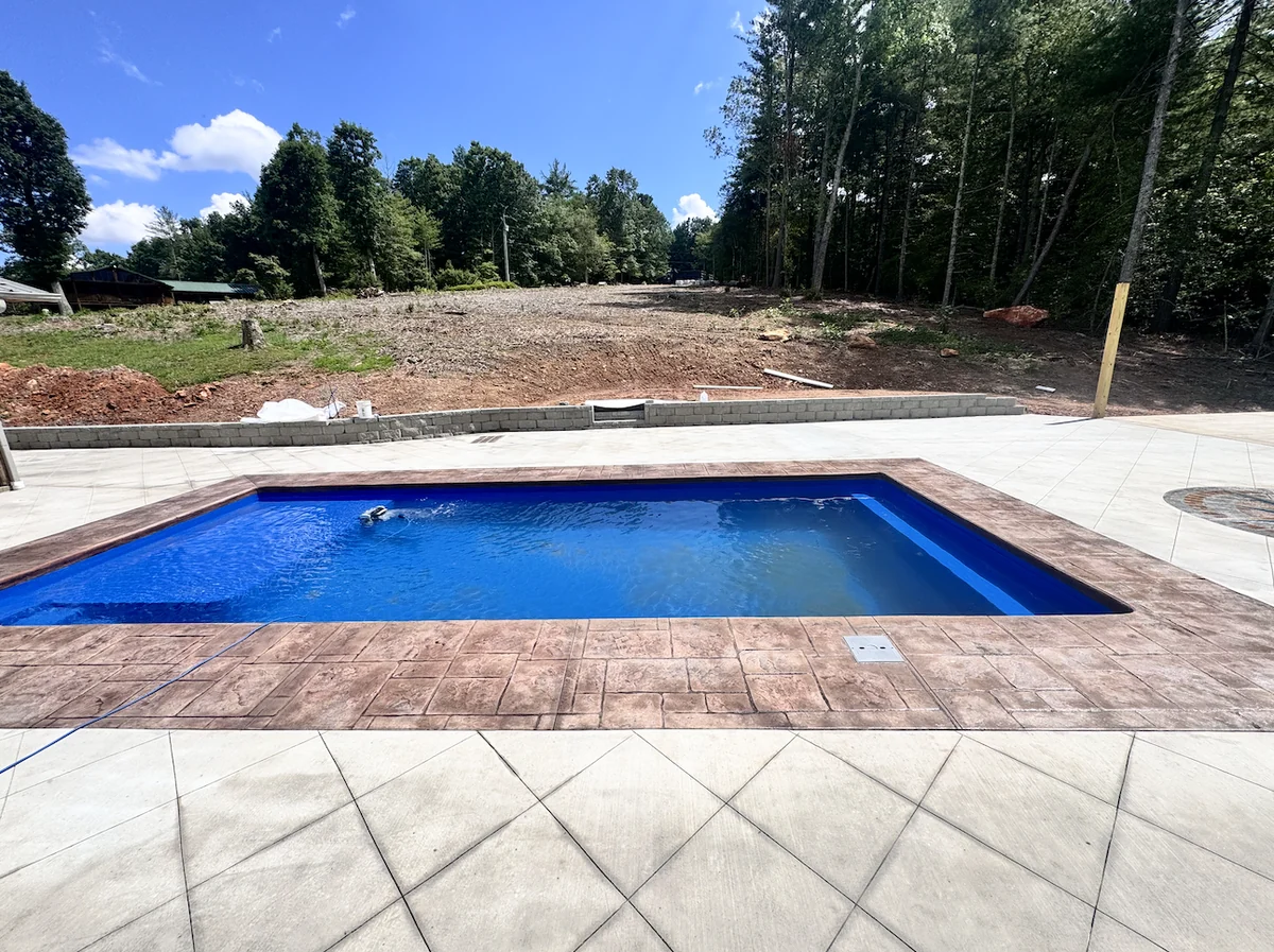 Rectangular pool with stamped concrete coping and a wide diamond-scored concrete pool deck at a newly cleared Foothills home site &mdash; The Concord Concrete Company