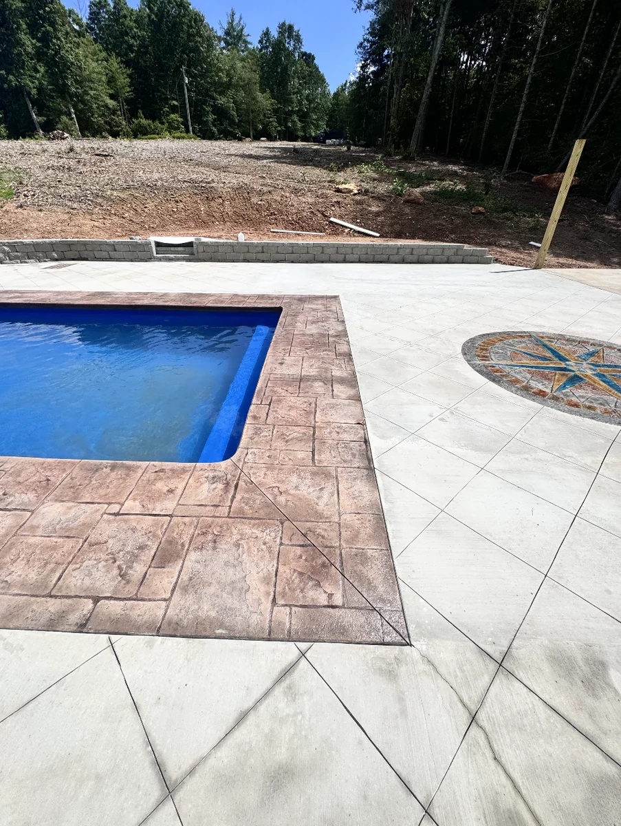 Close view of stamped ashlar-pattern pool coping in warm rust tones meeting a diamond-scored concrete deck &mdash; The Concord Concrete Company